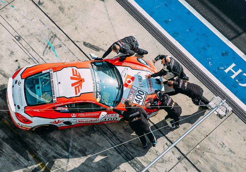 Five crew members push a red and white race car with the number 400 on its hood in a pit lane area at a racetrack. Five crew members push a red and white race car with the number 400 on its hood in a pit lane area at a racetrack.