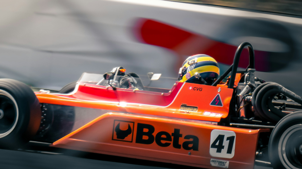 A racing driver wearing a helmet drives an orange open-wheel race car labeled "Beta" and number 41 on a racetrack.