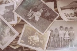 A collection of vintage black-and-white photographs showing children playing, posing, and outdoor scenes, scattered in a pile.