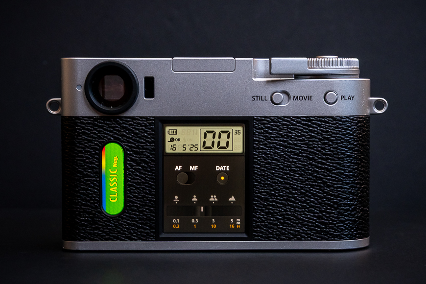 A digital camera with a textured black grip, LCD screen displaying settings, and labeled buttons for AF, MF, and DATE on the back panel.