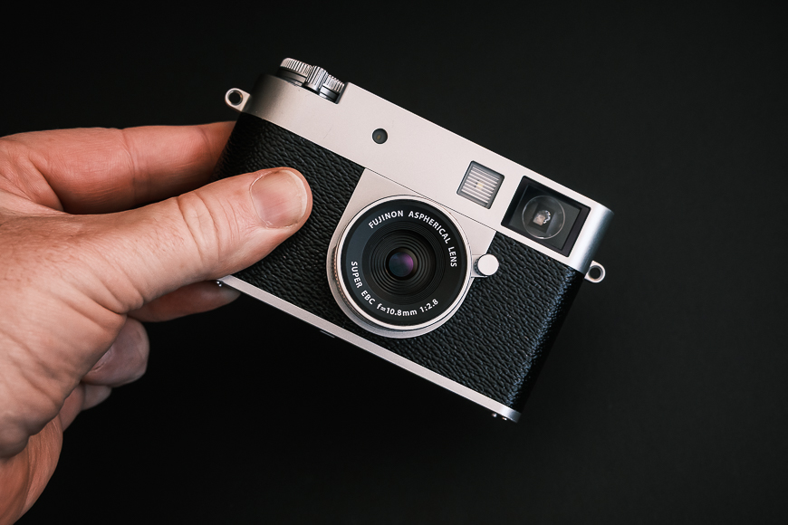 A hand holds a vintage-style digital camera with a silver and black body against a plain black background.