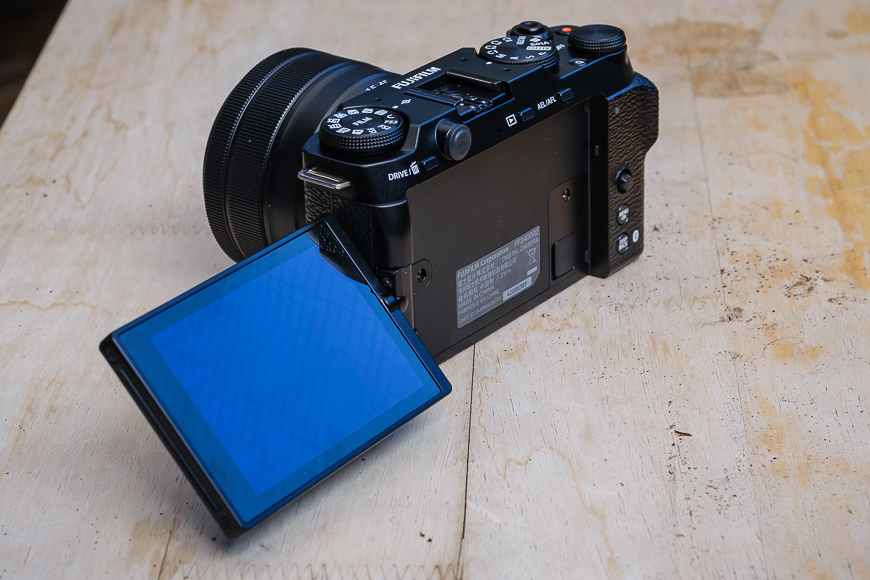 A black camera with a tiltable LCD screen is open on a wooden surface.