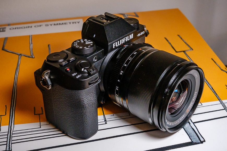 A fujifilm camera with a lens attached, resting on a patterned surface.
