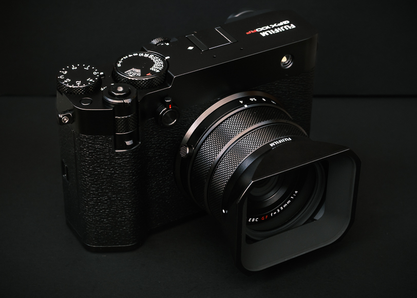 A black Fujifilm digital camera with a large lens and various controls rests on a black surface.