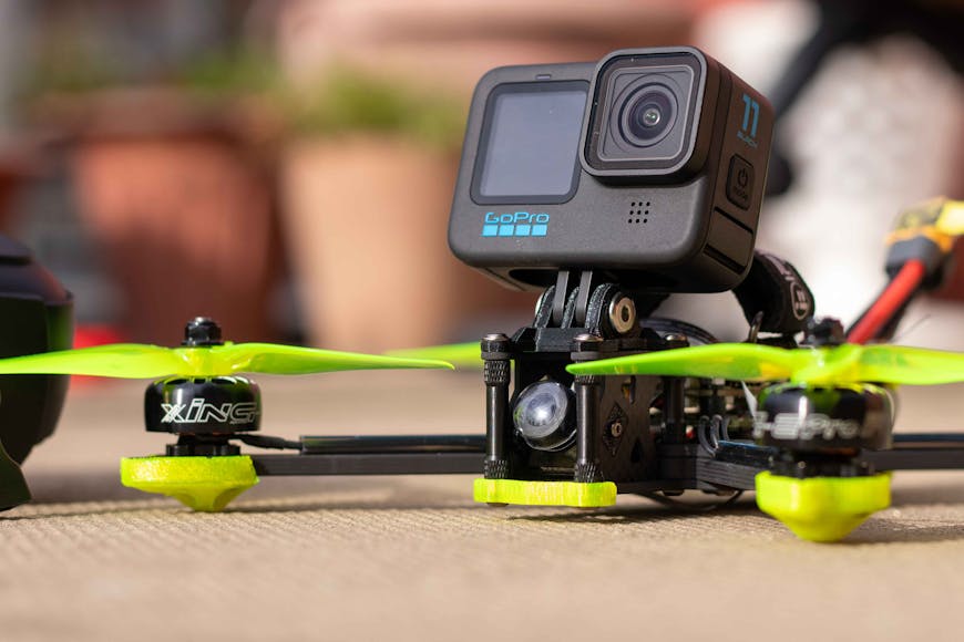 A GoPro camera mounted on a racing drone with neon green propellers, placed on an outdoor surface.