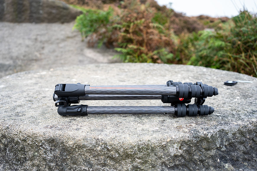 A folded tripod rests on a flat stone surface outdoors.