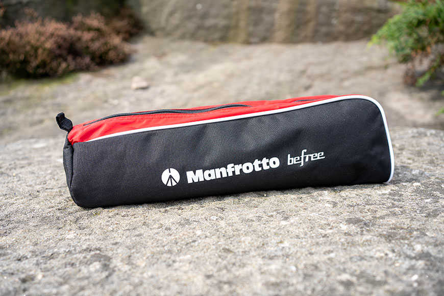 A Manfrotto Befree tripod bag, black with white logo, lies on a rock surface outdoors.