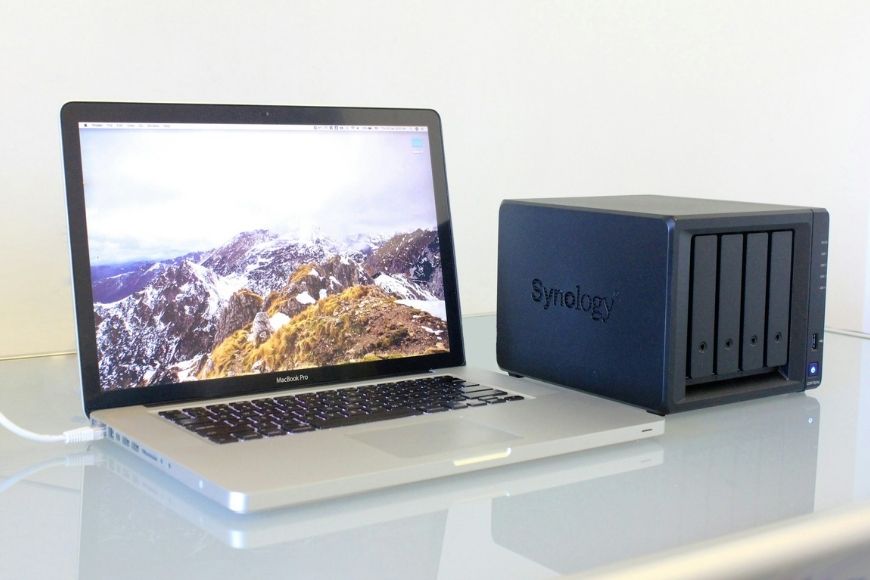 A laptop next to a synology nas device on a desk.