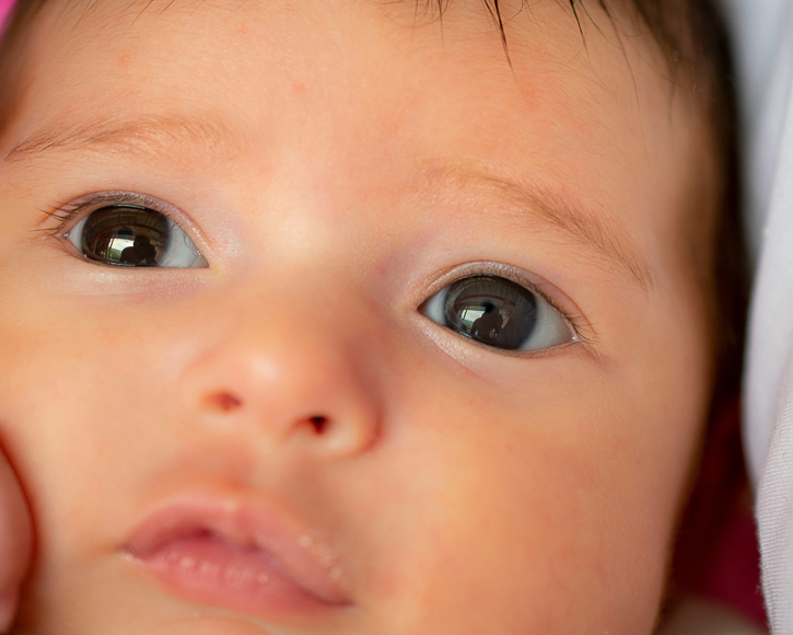 Close-up of a baby's face showing wide-open eyes, nose, and mouth with soft lighting and a neutral expression.