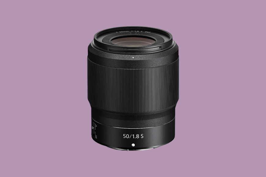 A black camera lens marked "50/1.8 S" stands upright against a solid lavender background.