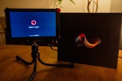 A small tablet with a tripod stand displays a screen with "OBSbot Tablet" text. Next to it is a black folder with a red and yellow abstract design.