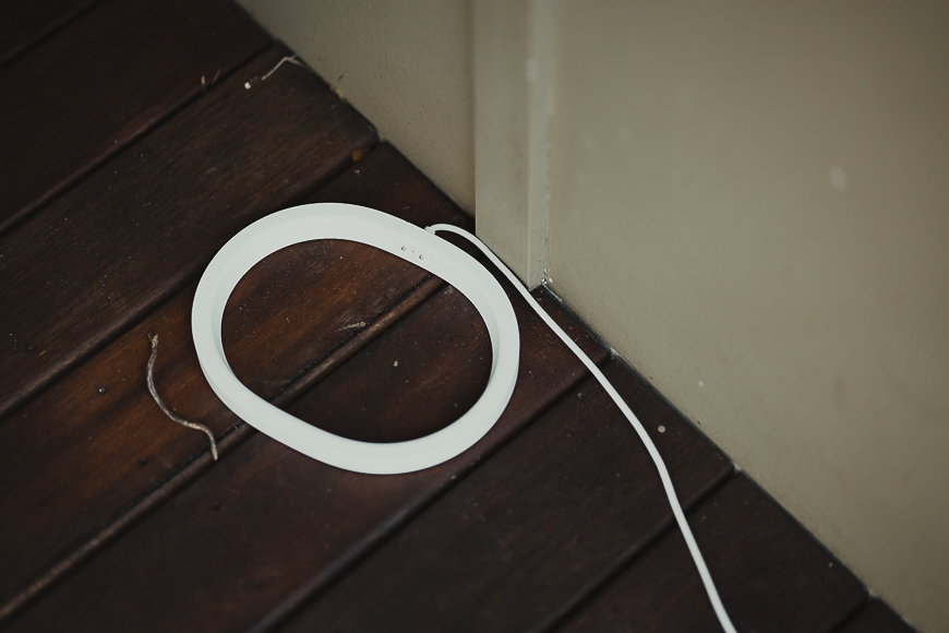 A white circular object with a cord lies on a dark wooden floor near a beige wall corner.