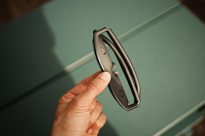 A hand holding a pair of black, foldable sunglasses against a greenish background.
