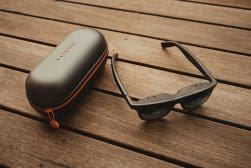 A pair of black smart glasses and a Viture-branded carrying case rest on a wooden surface.