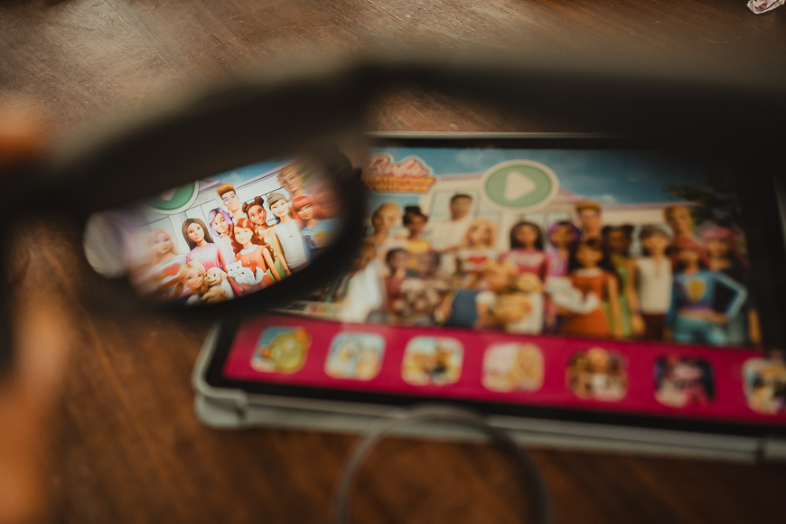 A tablet screen displays a group image of animated characters, viewed through a pair of eyeglasses, with the glasses bringing the characters into focus.