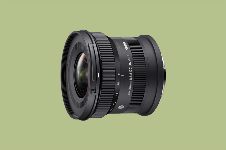 A black Sigma 10-18mm f/2.8 DC DN camera lens on a light green background.