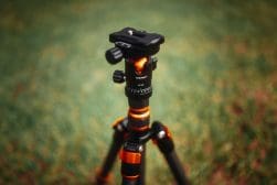 An orange and black tripod sits on a grassy field.